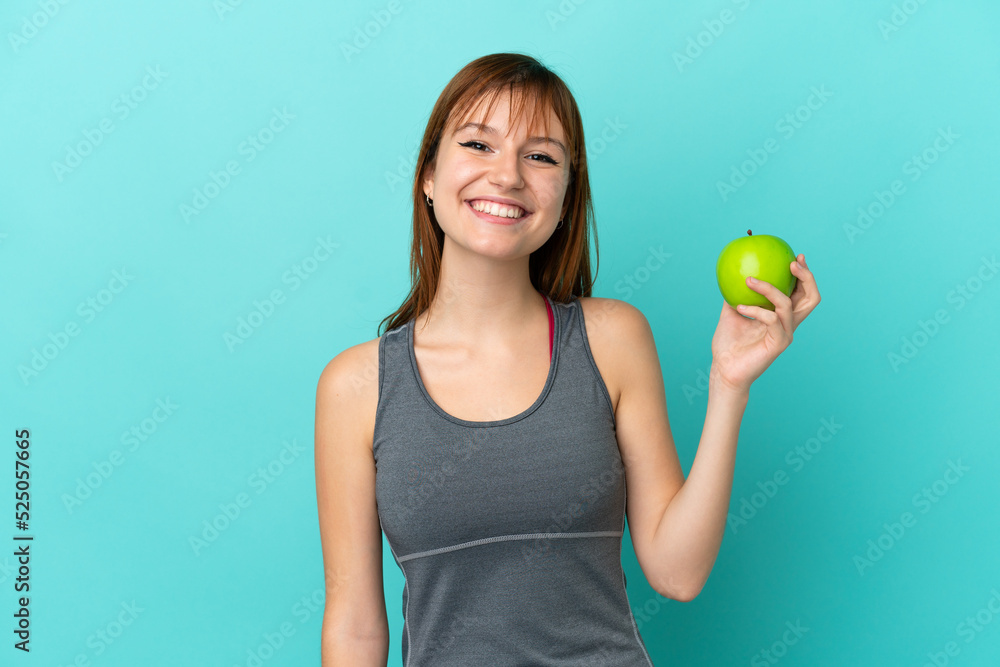 Redhead girl isolated on blue background with an apple and happy Redhead girl isolated on blue background with an apple and happy