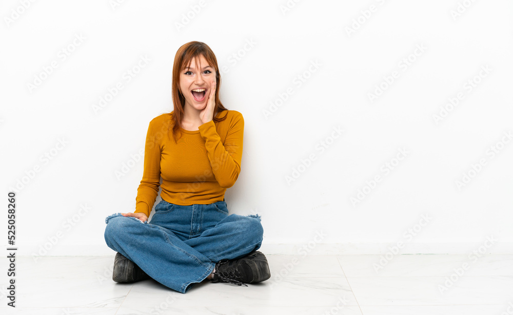 Redhead girl sitting on the floor isolated on white background with surprise and shocked facial expression Redhead girl sitting on the floor isolated on white background with surprise and shocked facial expression