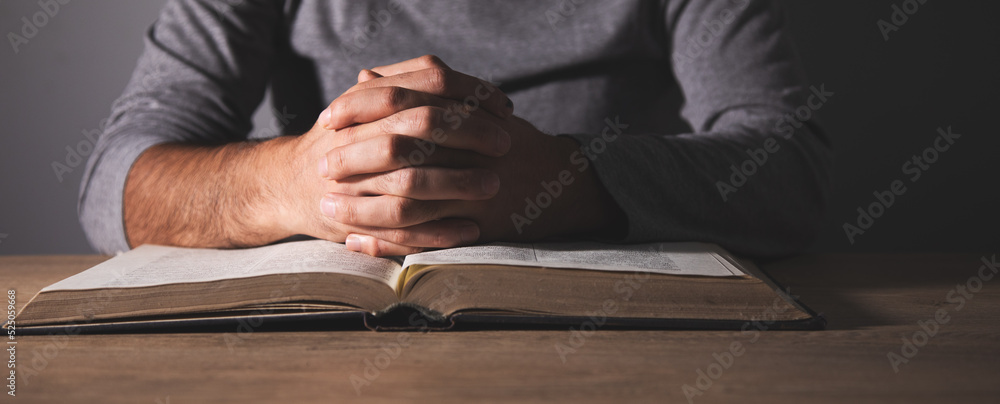 Hands of a man praying over a Bible