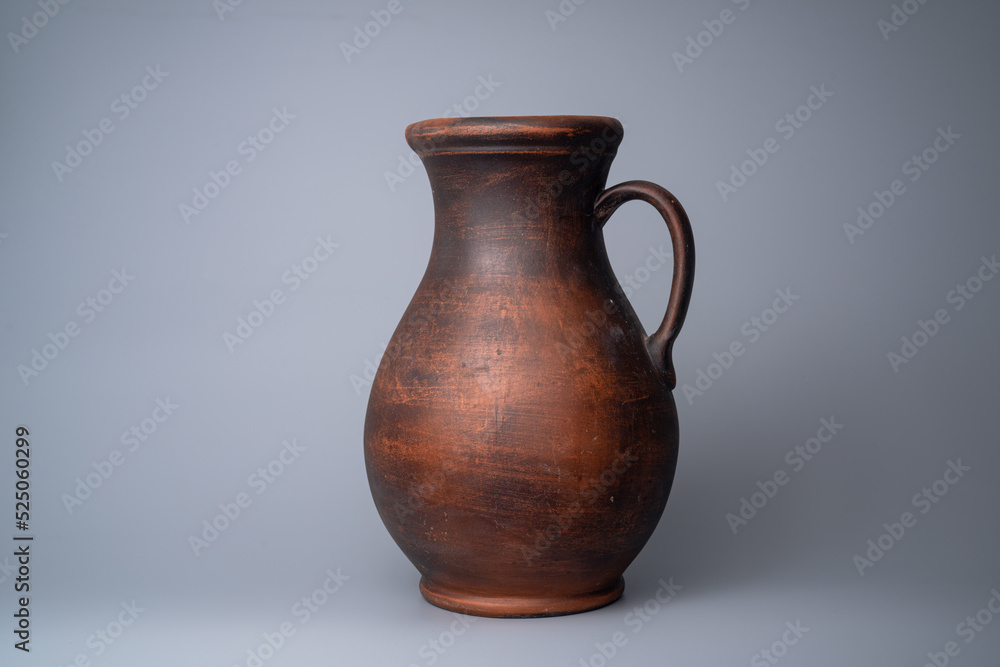 Dark brown jug with a handle, handmade jar from clay on a gray background in the studio. Earthenware for drink and food. Kitchen utensils. Old rustic cookware made of earthen. Retro craft vessel.