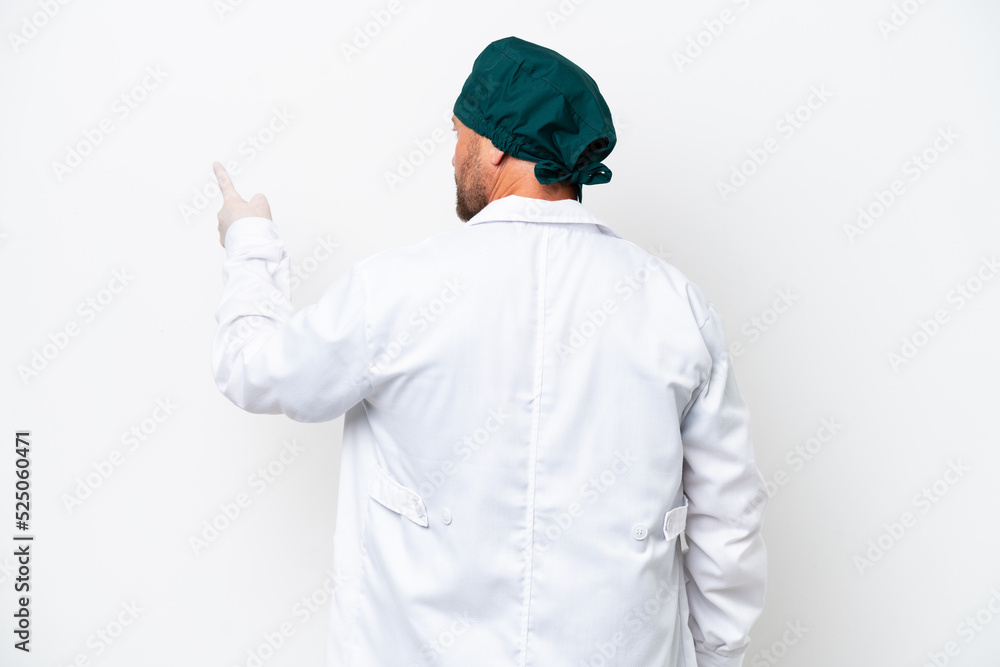 Middle age surgeon in green uniform isolated on white background pointing back with the index finger