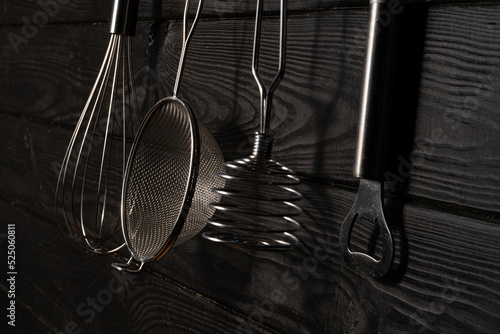 Opener, whisk, masher and strainer hanging against grey wall in a restaurant or home kitchen. Kitchen utensils made of stainless steel or metal. Set of tools for cooking food. Kitchenware on drainer. photo