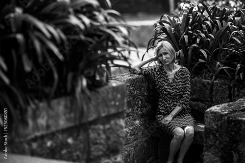 A middle-aged woman sits on a stone bench in old park. Black and white photo.