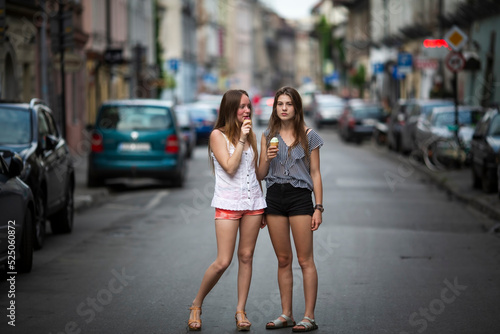 Two girlfriends are walking around town in the summer and eating ice cream.