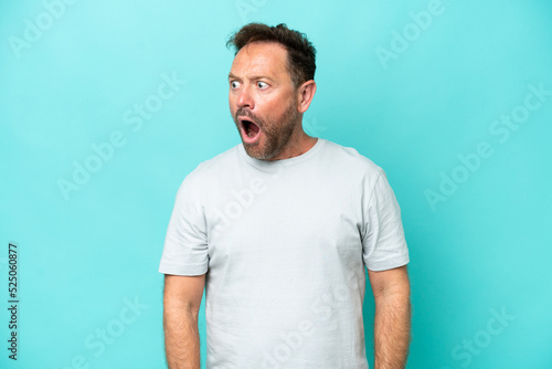 Middle age caucasian man isolated on blue background doing surprise gesture while looking to the side