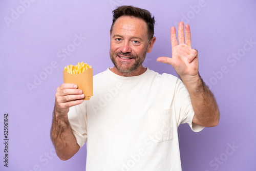 Middle age caucasian man holding fried chips isolated on purple bakcground happy and counting four with fingers © luismolinero
