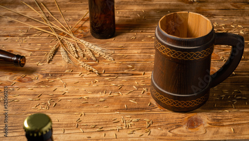 Oak mug with a handle and a glass brown bottle on a wooden table in a pub or bar. Handmade wooden tankard for beer or kvass. Brown mug with ornament, wheat grains and spikelet on a wooden surface.