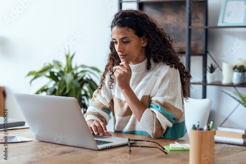 Картината върху платно Concentrated beautiful business woman working with laptop while drinking coffee in living room at home