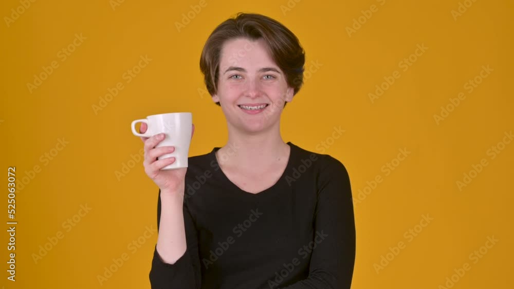 Young happy girl posing on a yellow studio background. Woman hold paper cup of coffee or tea drinking. People lifestyle concept. Young happy girl posing on a yellow studio background. Woman hold paper cup of coffee or tea drinking. People lifestyle concept.