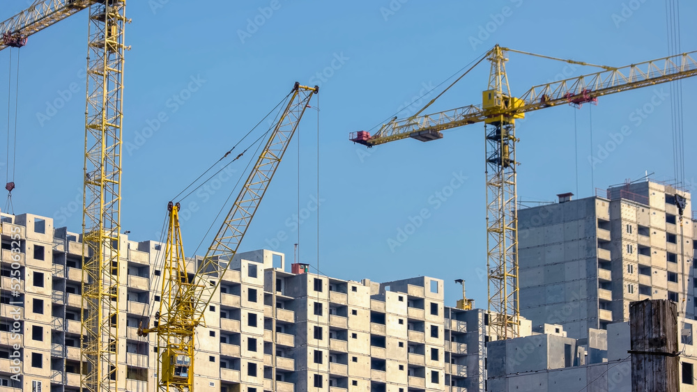 Yellow construction cranes and buildings over blue sky background. High-rise skyscrappers under construction.