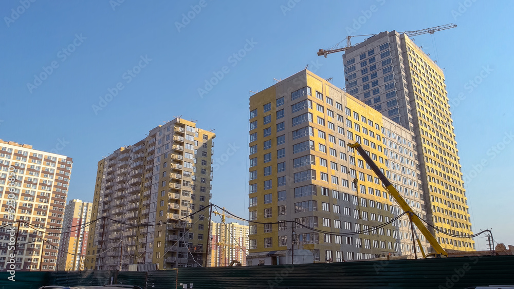 Many high-rise buildings and yellow construction crane. Blus sky background.