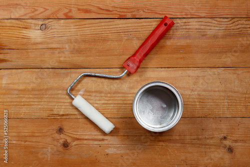 Paint roller and empty metal can on wooden background. View from above.