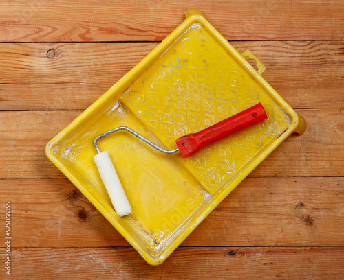 Paint roller in an empty plastic tray. On wooden boards