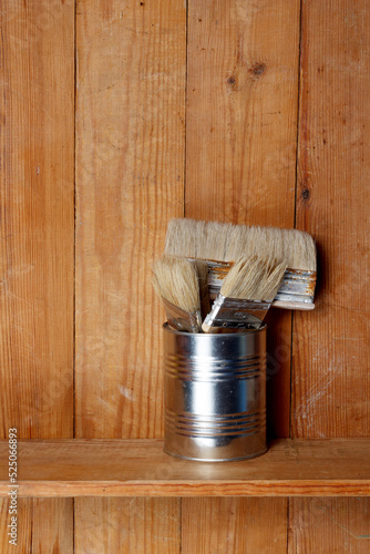 Paint brushes in a tin on a wooden shelf