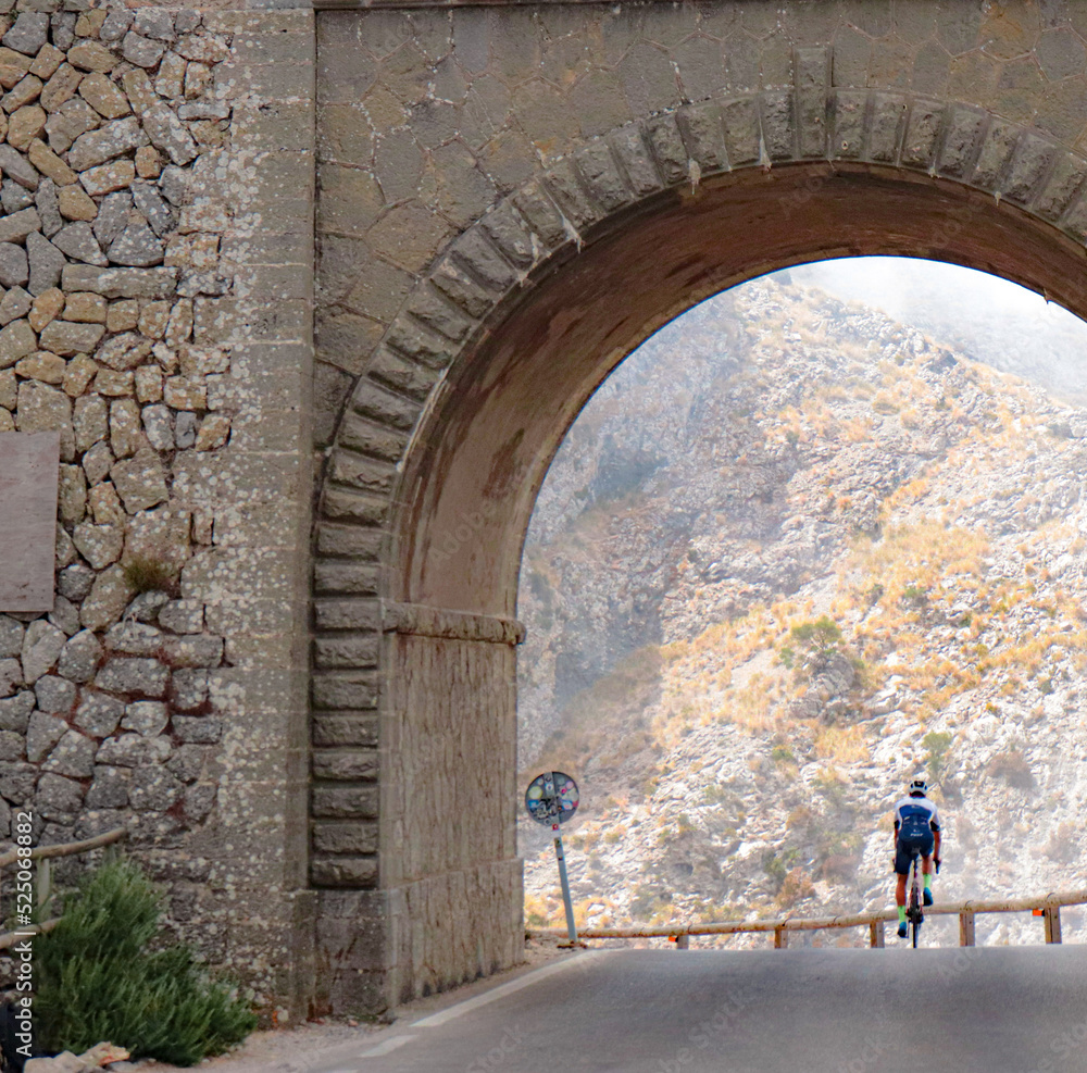 bridge in mallorca on the tie knot road with a cyclist riding down the road with the mountains in the background