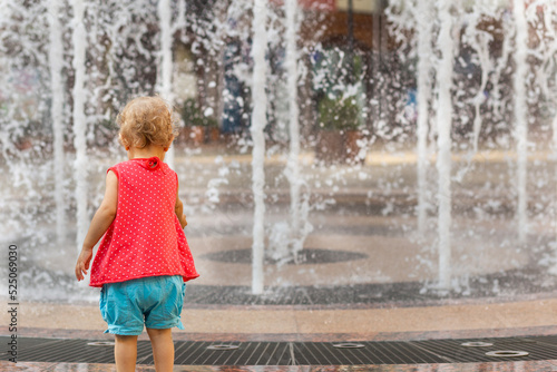 Little girl stretches her hands to the blurred fountain