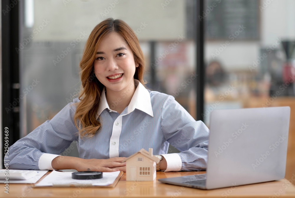Miniature house in the hands of an Asian woman real estate agent home loan working at the office. Looking at the camera. Miniature house in the hands of an Asian woman real estate agent home loan working at the office. Looking at the camera.