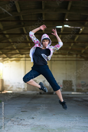 Young female hip hop dancer dancing and jumping in abandoned building on a sunny summer day	
