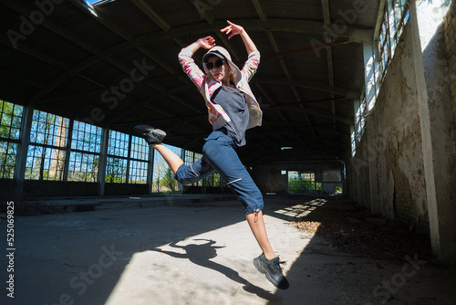 Young female hip hop dancer dancing and jumping in abandoned building on a sunny summer day	
