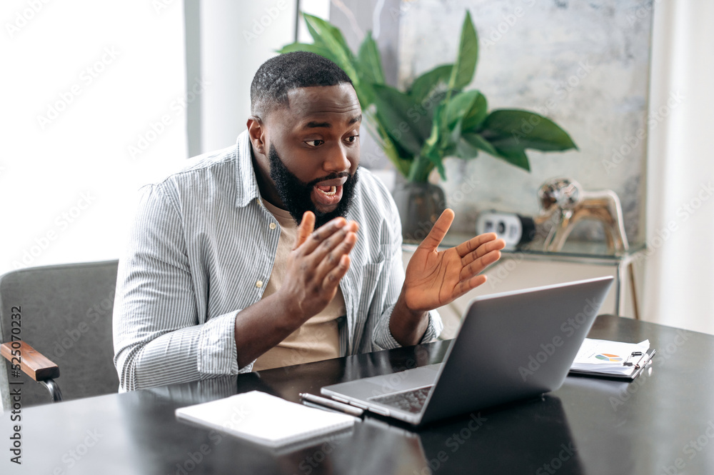 Online video meeting. Serious confident african american man, owner company, sales manager, sits on office, has business conversation with colleagues by video call using laptop, explain financial plan Online video meeting. Serious confident african american man, owner company, sales manager, sits on office, has business conversation with colleagues by video call using laptop, explain financial plan