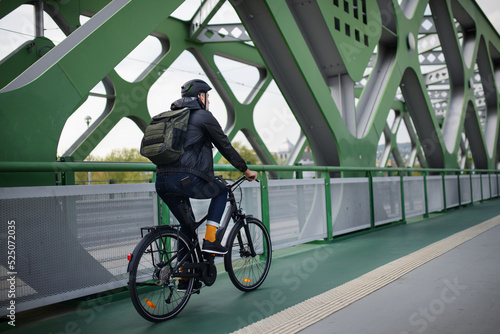 Fototapet Rear view of businessman commuter on the way to work, riding bike over bridge, sustainable lifestyle concept