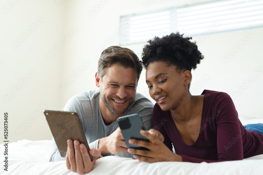 Image of happy diverse couple using smartphone and tablet and lying in bed Image of happy diverse couple using smartphone and tablet and lying in bed