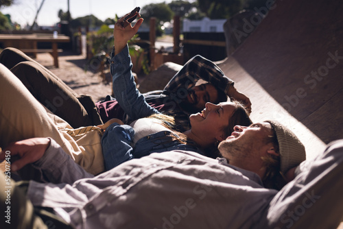 Image of happy diverse female and male friends with skateboards and smartphone in skate park photo