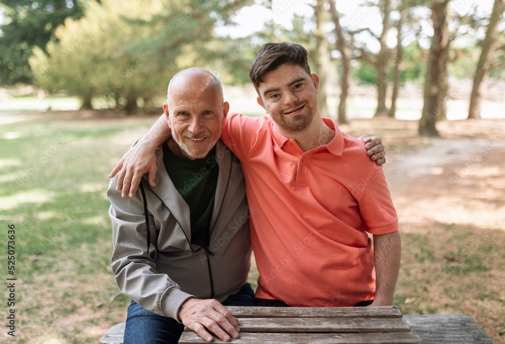 Happy senior father with his young son with Down syndrome embracing and sitting in park. Happy senior father with his young son with Down syndrome embracing and sitting in park.