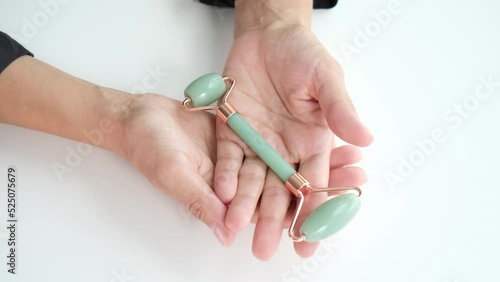Guasha masseurs are in the hands of a girl on a bright white marble background in a home light bath. Green jade, rose quartz gua sha. Different forms of skin care scrapers. photo