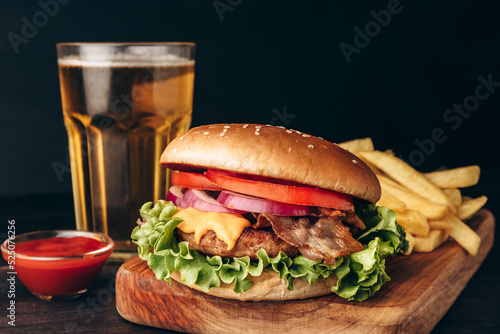 Food delivery burger hamburger with crispy bacon and potatoes fries and glass of beer on a dark background