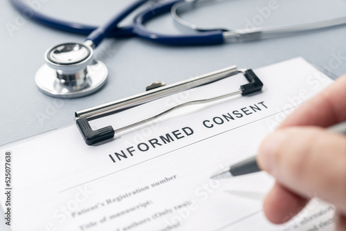 Hand filling a Informed Consent form and stethoscope on desk