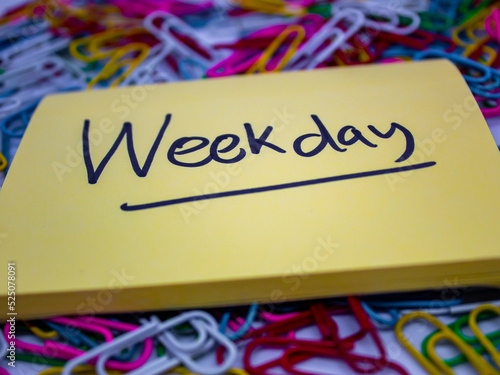 close-up selected focus yellow sticky notes with weekday underlined written on it or weekday writing on the sticky notes with colorful paperclip on the background in the office