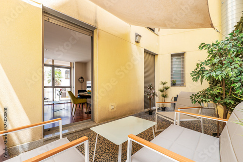 Terrace of an urban residential house with stone floors  glass and white metal furniture and artificial decorative plants and access to a living room with furniture