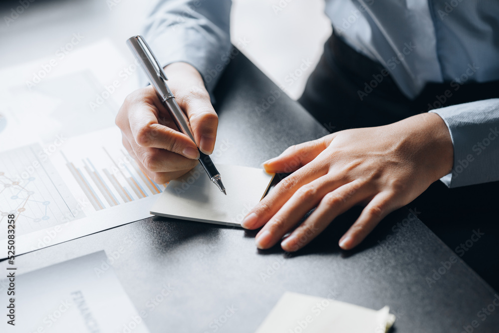 Businessman takes notes in a note paper, owns a startup company, sits in his office and checks the company's financial summary prepared by the finance department. Management concept of startup company Businessman takes notes in a note paper, owns a startup company, sits in his office and checks the company's financial summary prepared by the finance department. Management concept of startup company