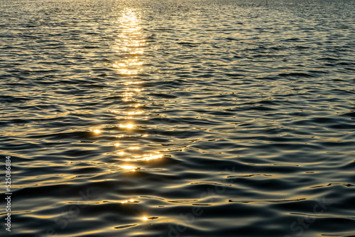 Linear golden sun glitter on rippled water surface of Aegean sea by sunset. Romantic atmosphere, abstract, background, texture. Selective focus, noise effect and grainy texture. 