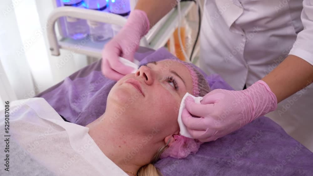 A beautician in pink gloves washes off a facial mask with wet wipes. Skin care. A beautician in pink gloves washes off a facial mask with wet wipes. Skin care.