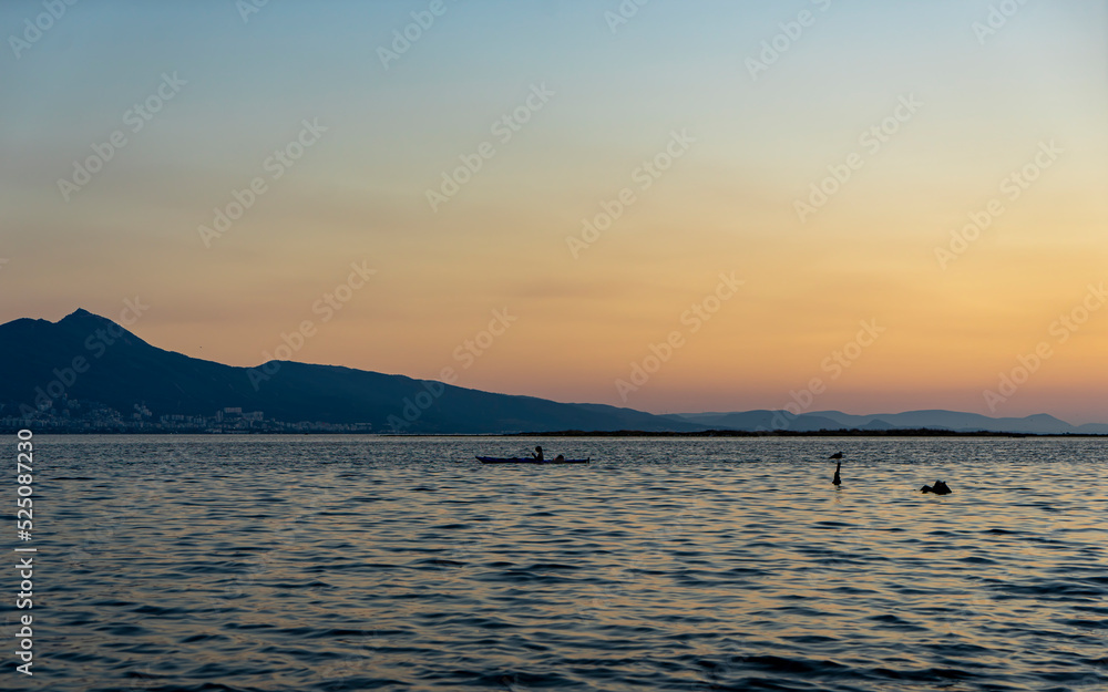woman is kayaking at beautiful sunset on İzmir Bay, Mavisehir, Karsiyaka. Canoeing in the bay against the city of Izmir. Canoe lessons and training.Selective focus, noise effect and grainy texture. 