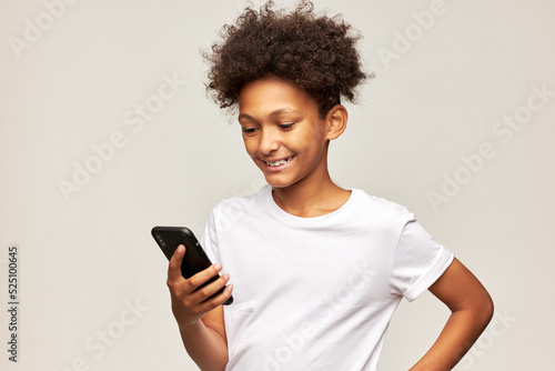 Cute african american boy kid in white mockup t-shirt chatting with his girlfriend looking at screen with smile, enjoying pleasant conversation, reading love message. Children and modern lifestyle
