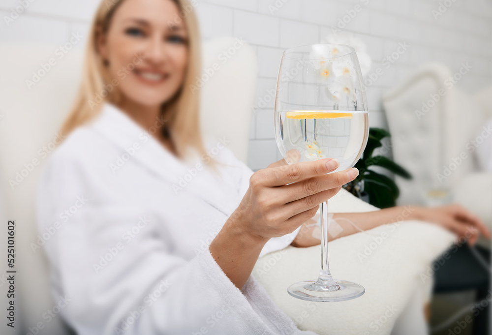 Beautiful woman with glass of refreshing lime drink during intravenous detox therapy with IV drip Infusion. Detox treatments at spa Beautiful woman with glass of refreshing lime drink during intravenous detox therapy with IV drip Infusion. Detox treatments at spa