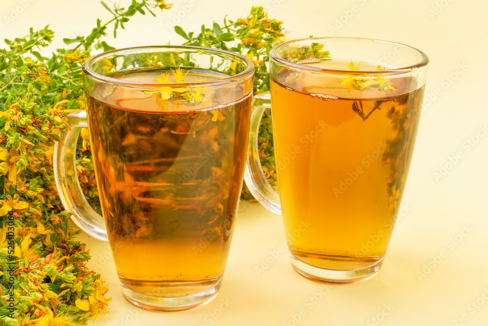 Two transparent mugs with tea (decoction, infusion) from the medicinal herb St. John's wort on a yellow background. Alternative medicine, herbs for health, herbal medicine. Two transparent mugs with tea (decoction, infusion) from the medicinal herb St. John's wort on a yellow background. Alternative medicine, herbs for health, herbal medicine.
