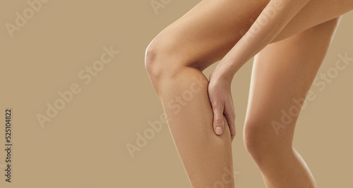 Woman feels a sudden leg cramp and touches her calf. Young lady suffers from pain due to a rare rheumatism symptom or torn, overstretched muscle after overtraining at a gym workout. Copy space banner © Studio Romantic