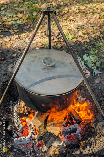 A cauldron covered with a lid in which kulesh is cooked hangs on a tripod over a fire