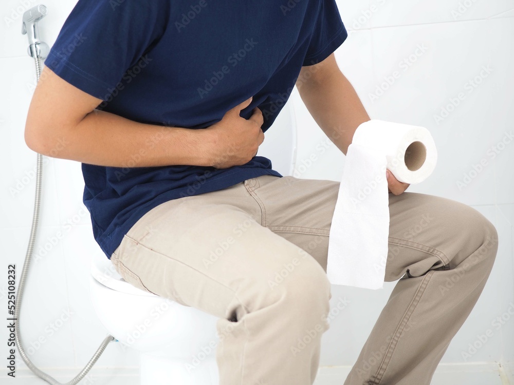 Young man sitting defecating from diarrhea in bathroom, stomachache, constipation. Health concept. Closeup photo, blurred.