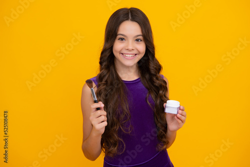 Beauty, make up and kids cosmetics. Teenage girl 12, 13, 14 years old with brush applying blush to face isolated on wellow background. Happy girl face, positive and smiling emotions. © Olena
