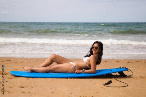Beautiful young woman lying and sunbathing on the surfboard on the shore of the beach. The woman is enjoying her trip to a paradise beach. Holiday and travel concept.