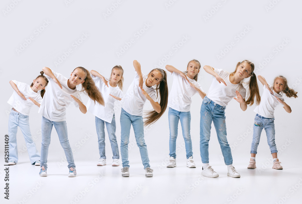 Obraz premium Dance group of happy, active little girls in jeans and t-shirts dancing isolated on white studio background. Concept of music, fashion, art, childhood, hobby