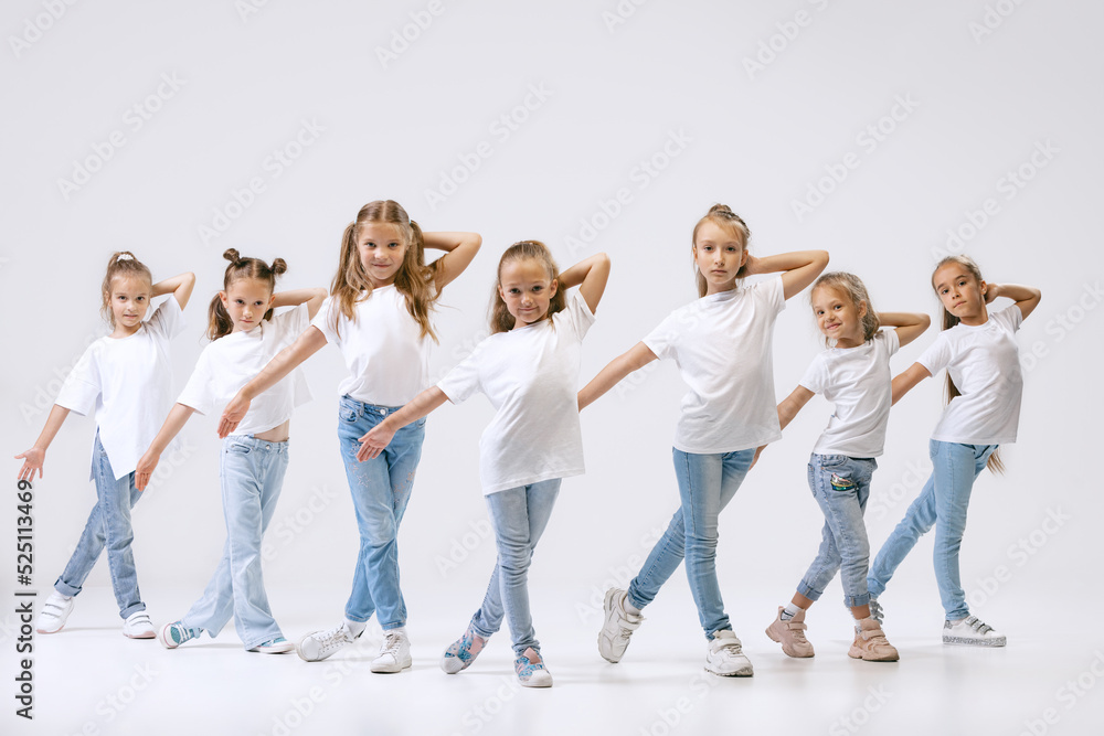 Fototapeta premium Active little girls, sportive kids in casual style clothes in motion isolated on white studio background. Concept of music, fashion, art, childhood, hobby