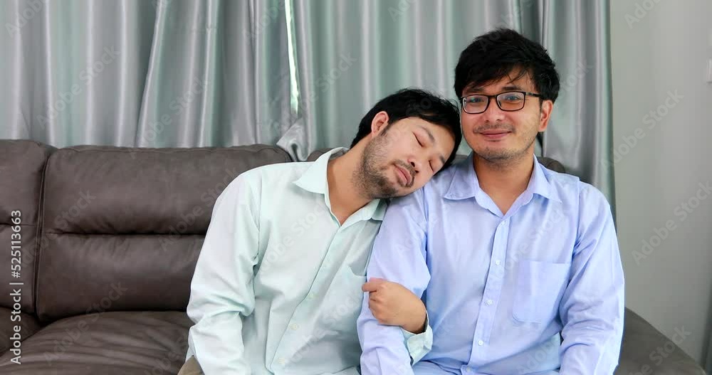 Happy homosexual male couple spending time together on sofas inside their homes.Happy together concept. Happy homosexual male couple spending time together on sofas inside their homes.Happy together concept.