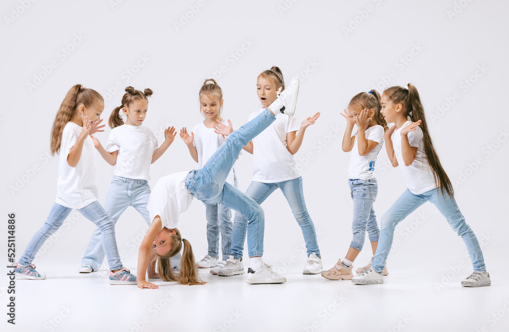 Naklejka premium Portrait of happy, active little girls, sportive kids in casual clothes dancing isolated on white studio background. Concept of music, fashion, art, childhood, hobby