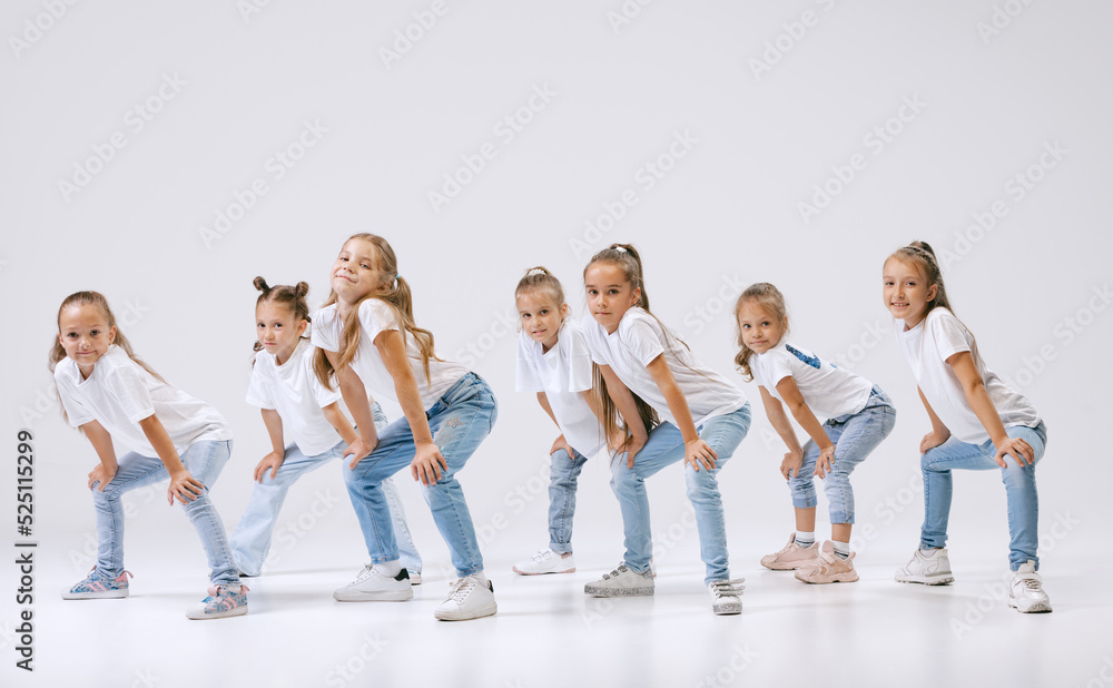 Obraz premium Portrait of happy, active little girls, sportive kids in casual clothes dancing isolated on white studio background. Concept of music, fashion, art, childhood, hobby